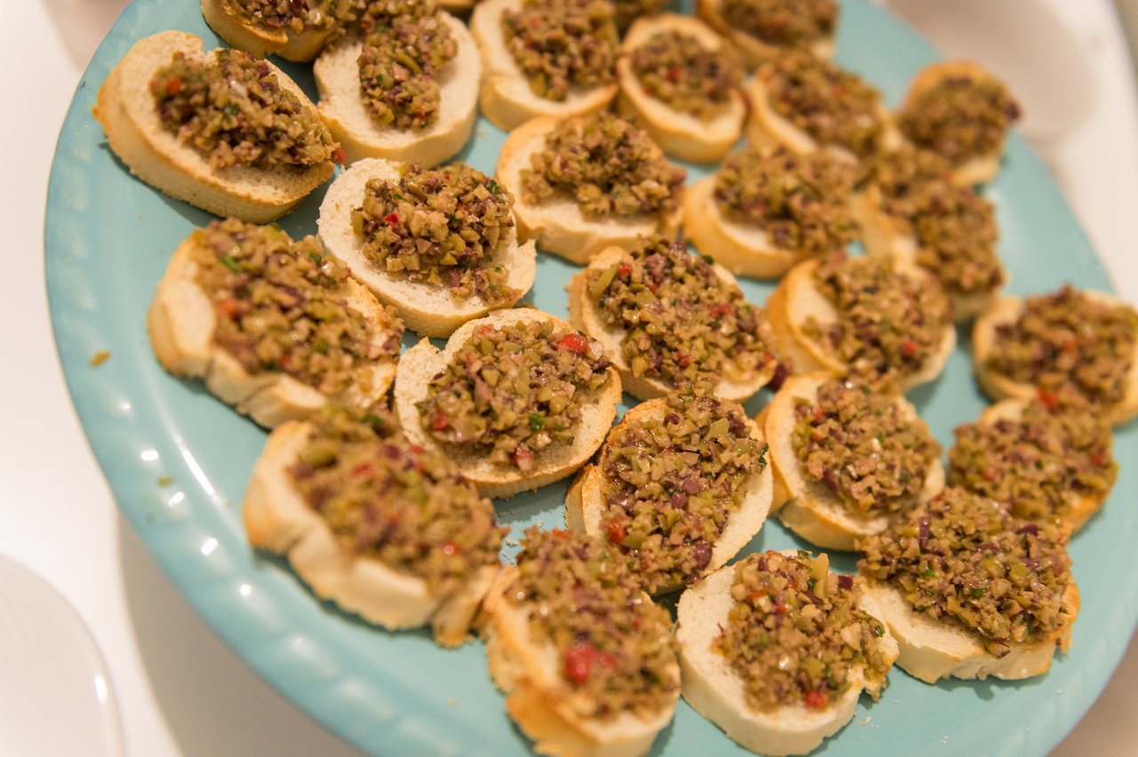 A plate of small toasted bread slices topped with finely chopped olives and vegetables, arranged for a party.