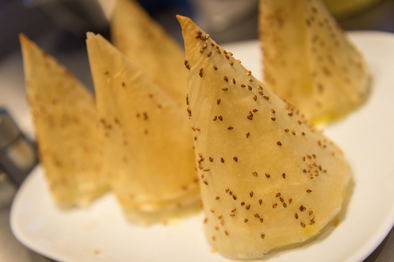 Several cone-shaped pastries with sesame seeds on a white plate, arranged for a New Year's Eve party.