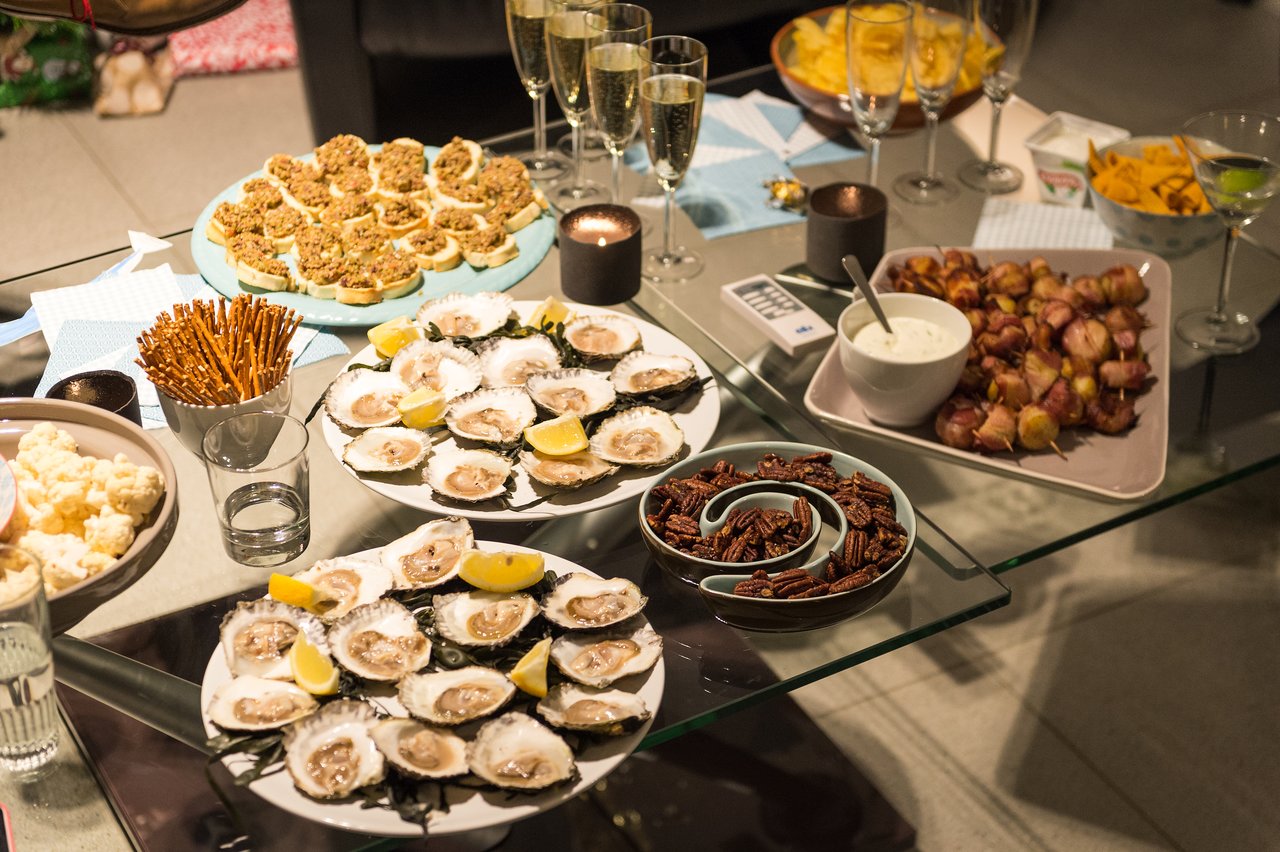 A table filled with party food, including oysters, appetizers, pretzels, and champagne glasses, set for celebration.