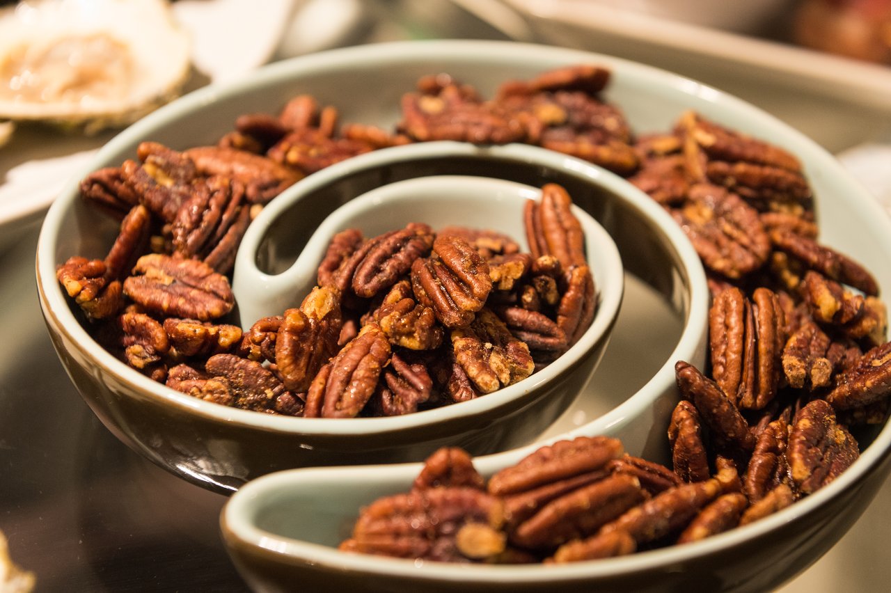 A decorative serving dish filled with roasted pecans at a party.