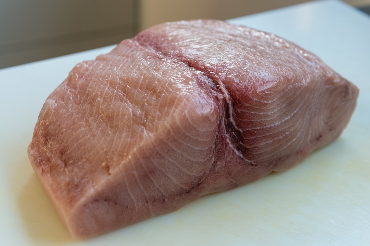 A raw tuna steak sits on a white cutting board, ready for preparation.