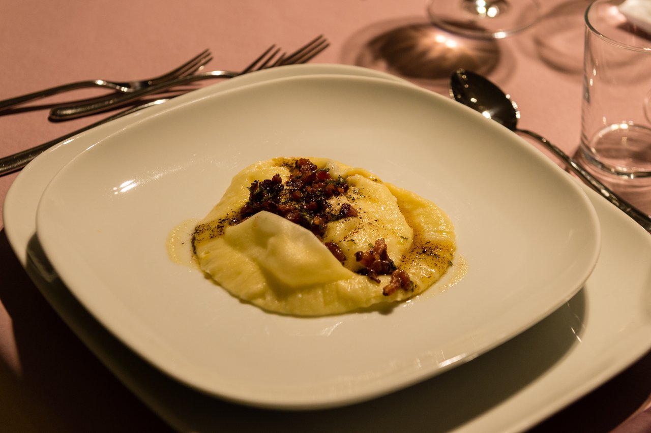 A plated ravioli dish with sauce and crispy toppings, served on a white plate at a formal dinner setting.