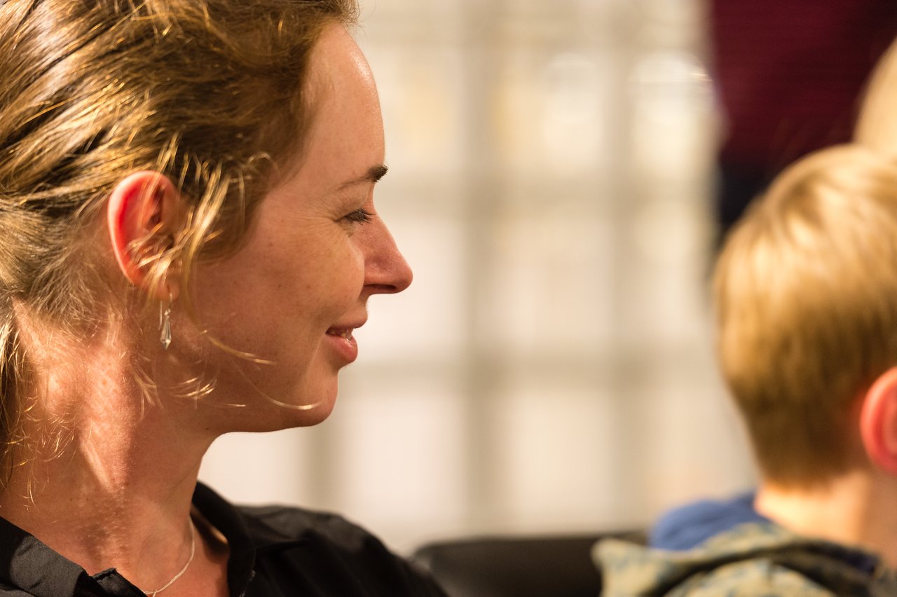 A woman in a black shirt smiles while looking at someone in a crowded party setting.