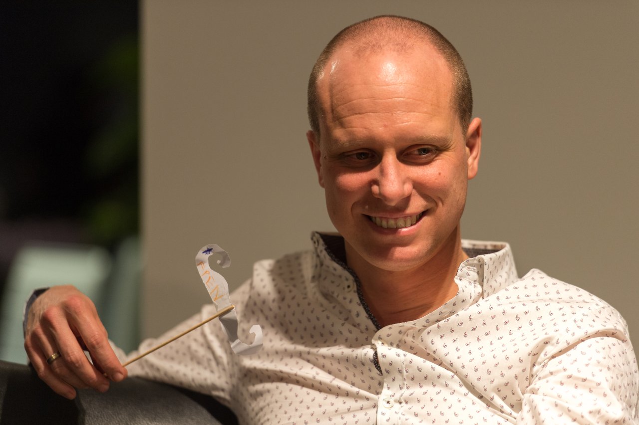 A man in a white patterned shirt smiles while holding a small decorative prop on a stick.