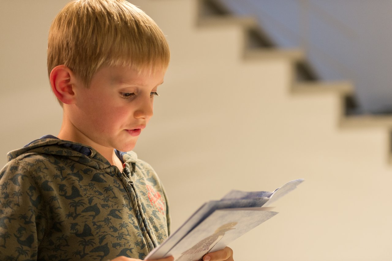 A young boy in a hoodie reads from a few sheets of paper at a New Year's Eve party.