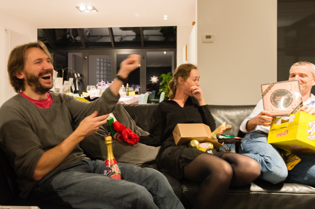 Three people sitting on a couch, laughing and exchanging gifts during a New Year's Eve celebration.