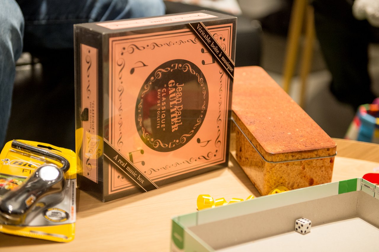 A table with a boxed perfume set, a tin container, a lighter, and a board game with dice.