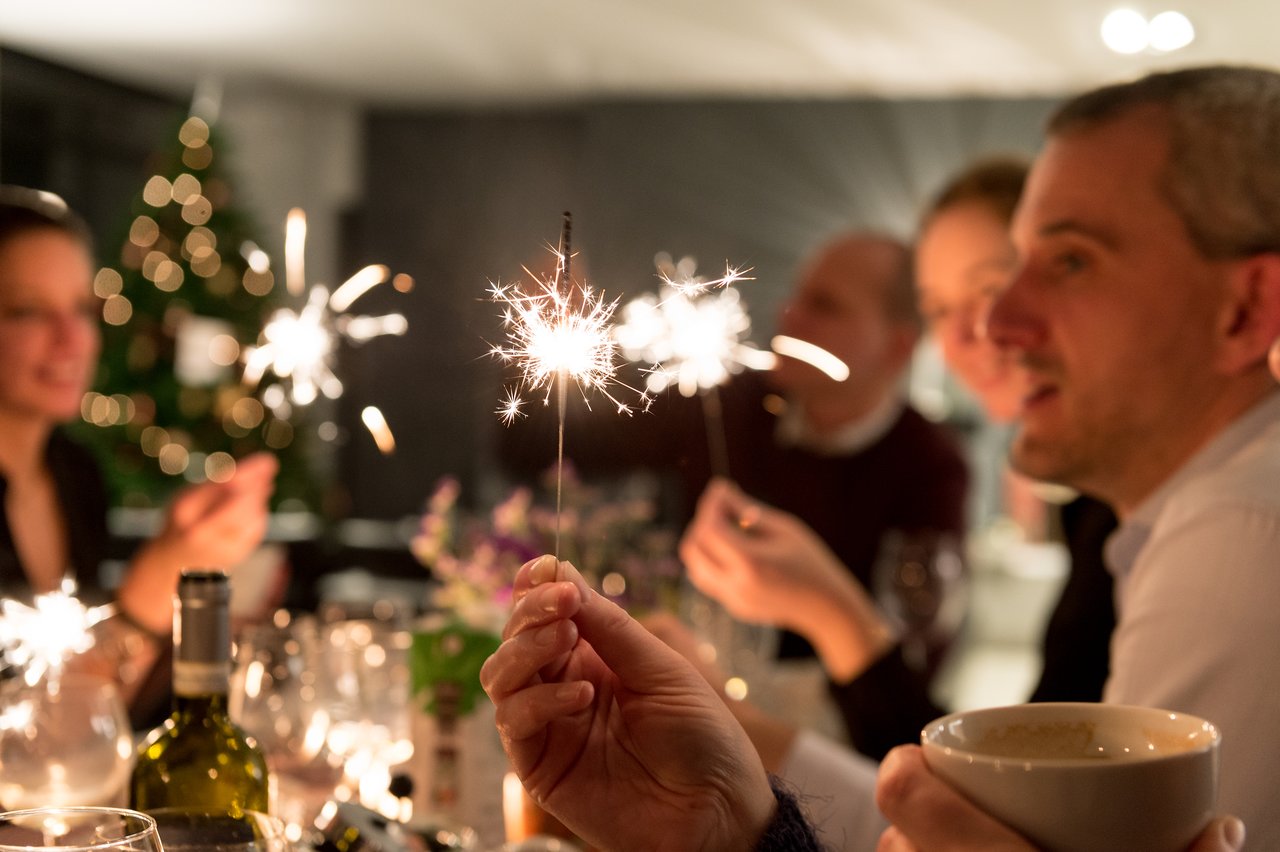 People celebrating New Year's Eve, holding sparklers and enjoying a festive gathering around a table.