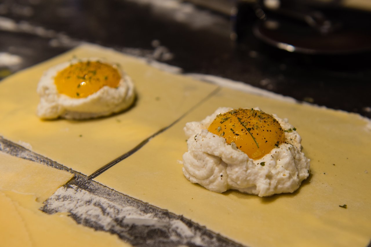 Two uncooked ravioli pieces with ricotta cheese and egg yolk filling on a floured surface, ready for preparation.