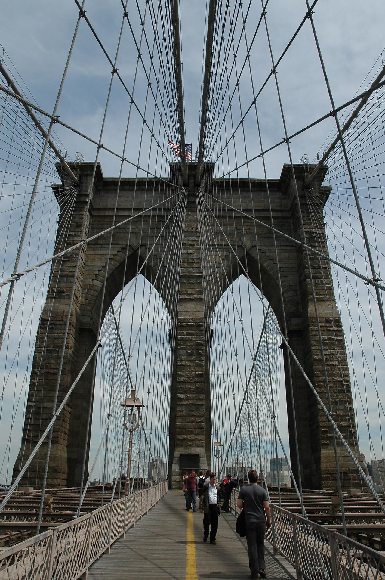 People walking on the pedestrian path of the Brooklyn Bridge, surrounded by suspension cables and stone arches.