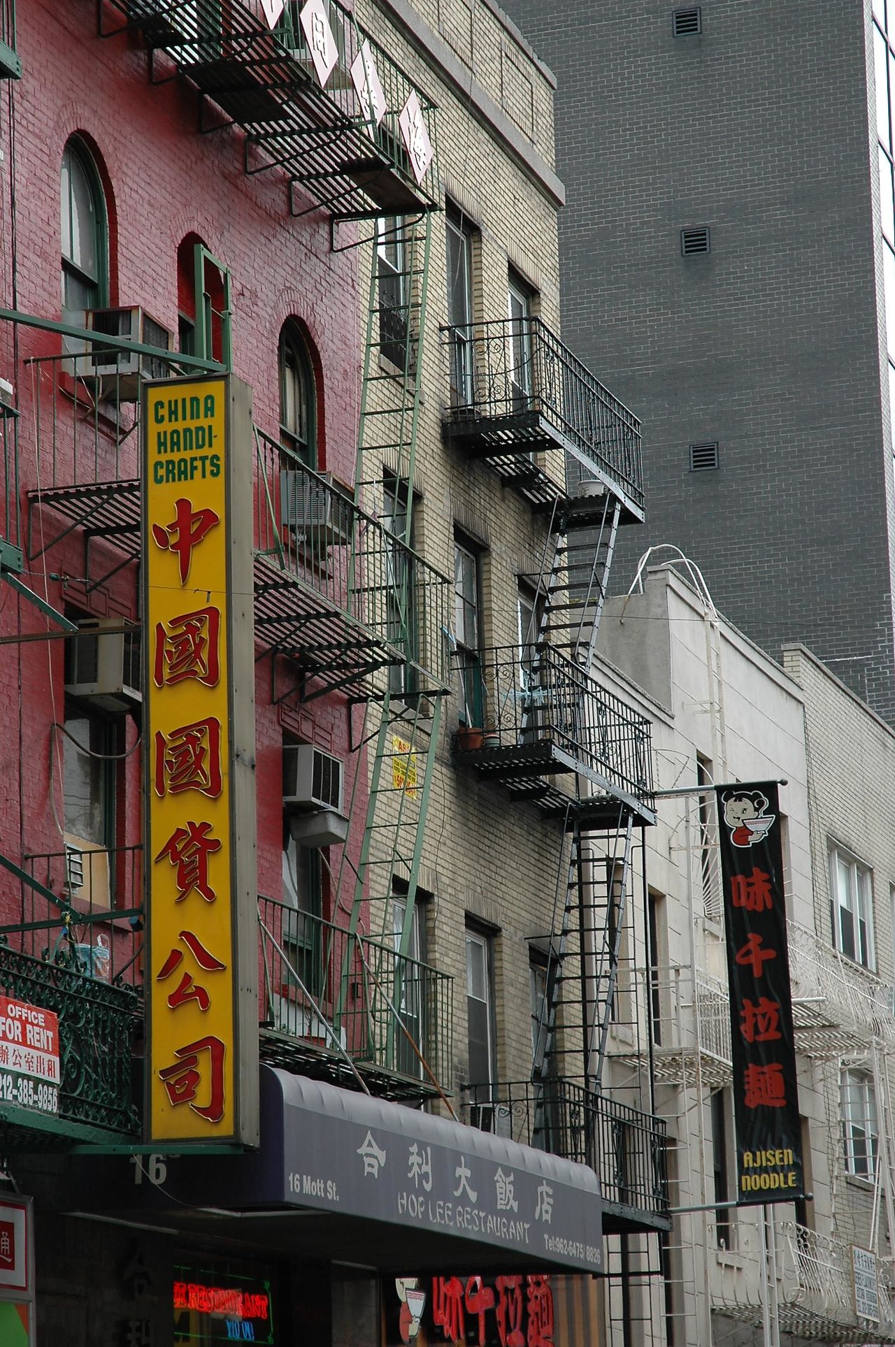 Storefronts and fire escapes on a busy Chinatown street, with colorful signs in English and Chinese.