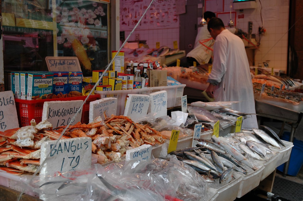 A seafood market vendor in Chinatown arranges fresh fish and crab legs on ice for sale.