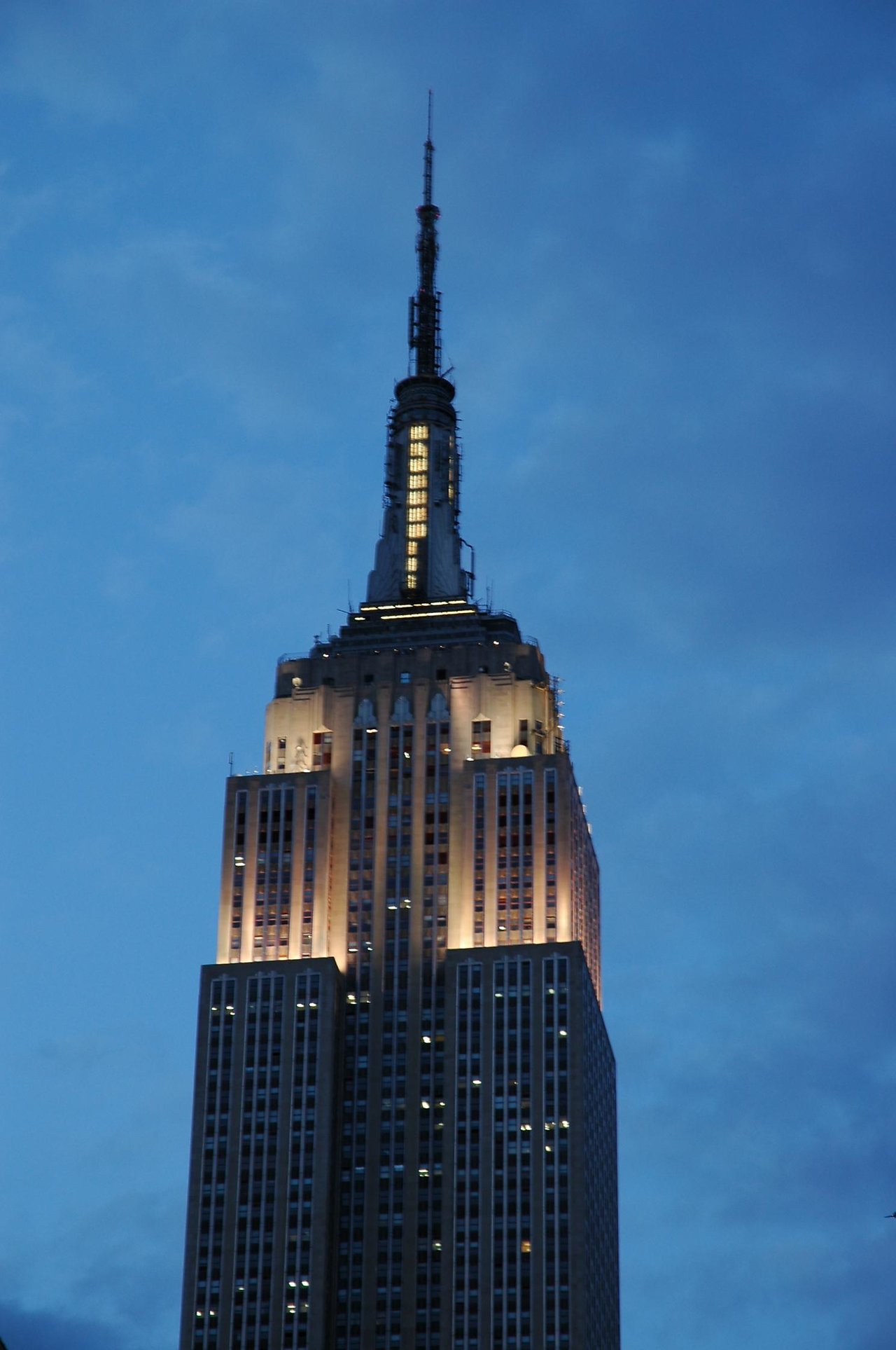 The Empire State Building at dusk, with its lights on against a blue sky.