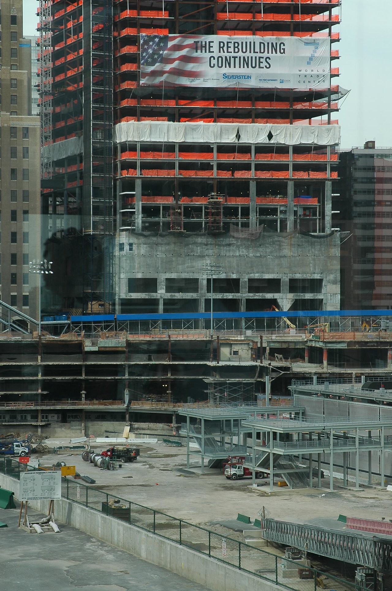 Construction site at Ground Zero with partially built structures and a banner reading "The Rebuilding Continues" on a building.