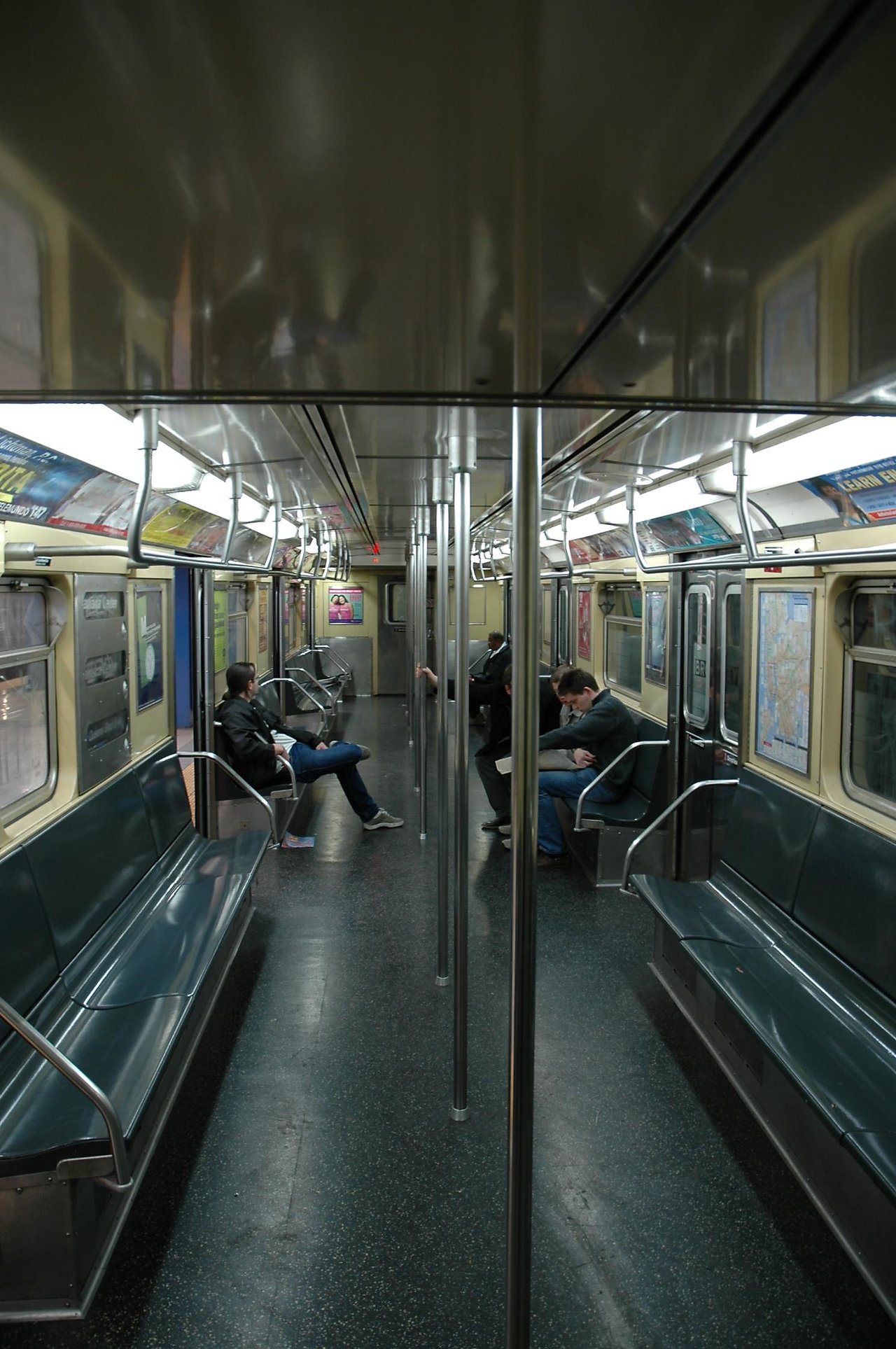 A few passengers sit on a mostly empty subway train, some reading or looking at their phones.