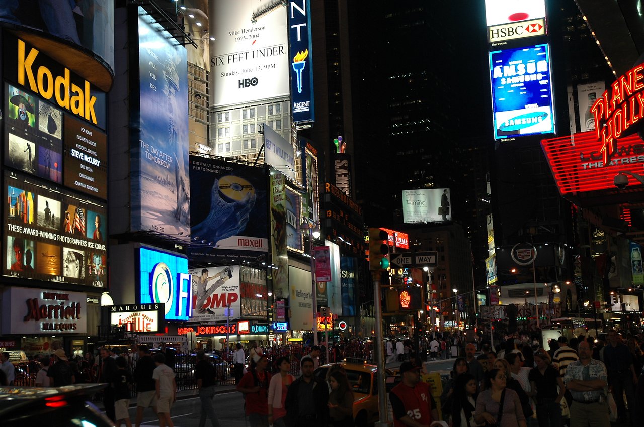 Crowded Times Square at night with bright billboards, neon signs, and people walking on the streets.