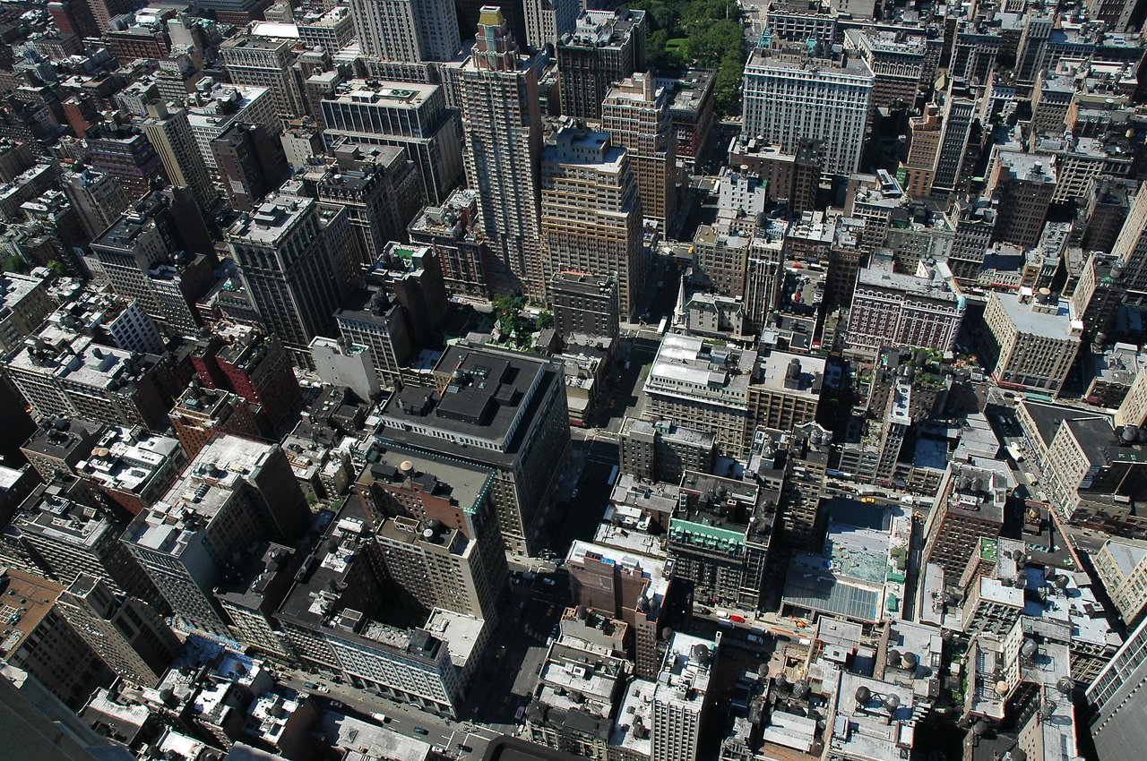 Aerial view of a dense cityscape with many tall buildings, streets, and rooftops in New York City.