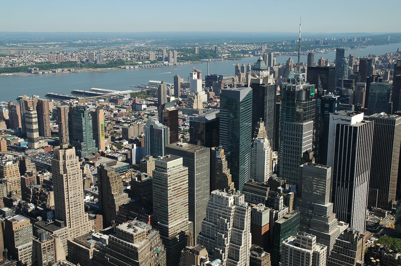 Aerial view of New York City skyscrapers with a river and distant buildings in the background.