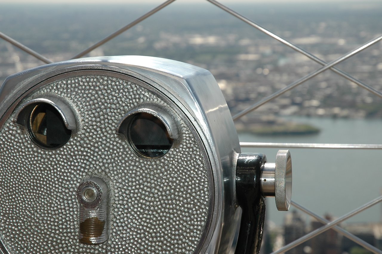 A coin-operated viewing telescope with a cityscape and water in the background.