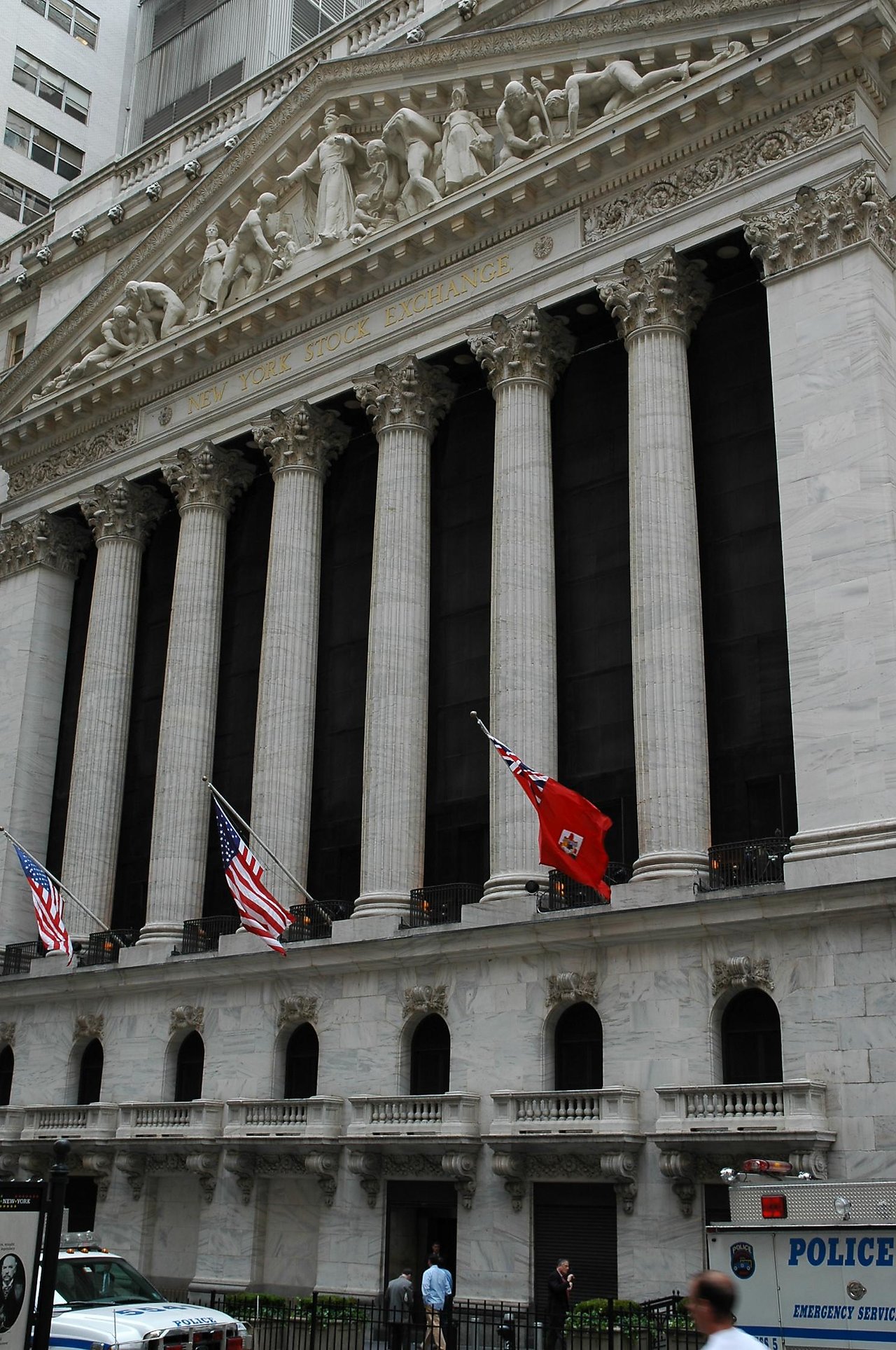 The New York Stock Exchange building with tall columns, American flags, and a police vehicle in the foreground.