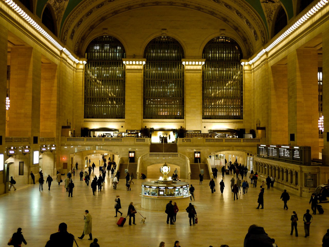 Grand Central Terminal's main hall with people walking, a central information booth, and large windows in the background.