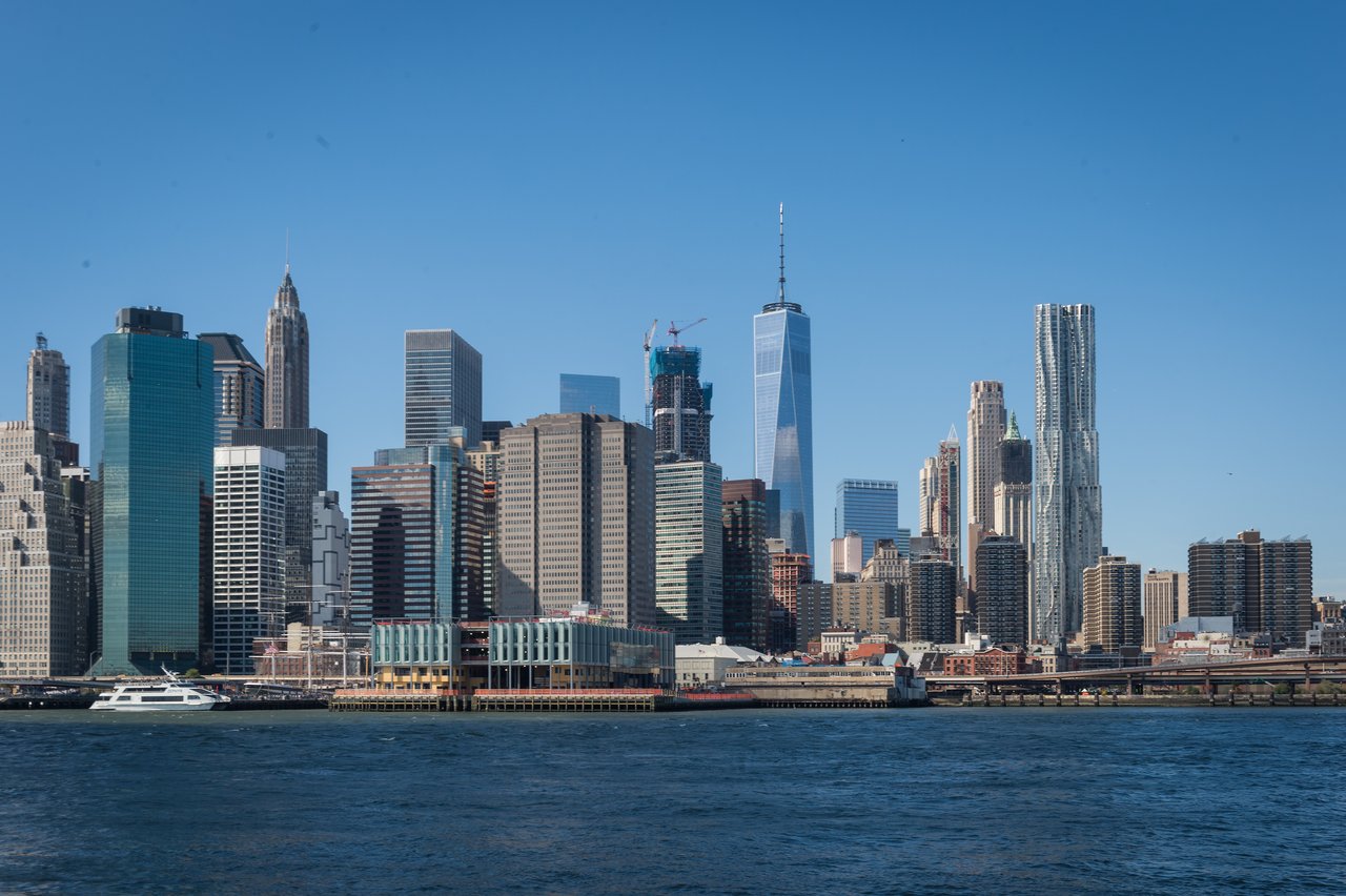 The Manhattan skyline with tall buildings and water in the foreground.