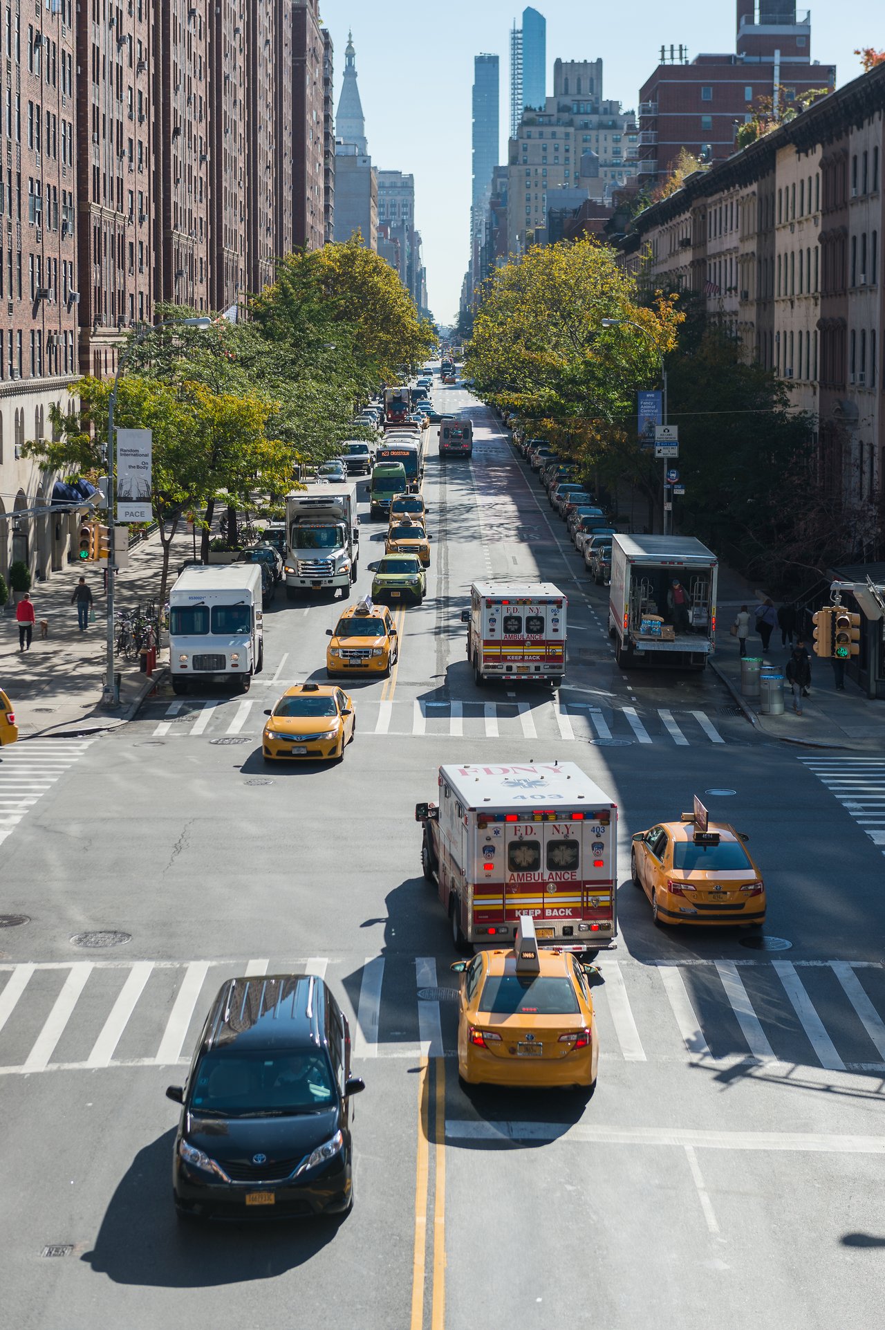A busy New York street with cars, taxis, and an ambulance driving through an intersection.