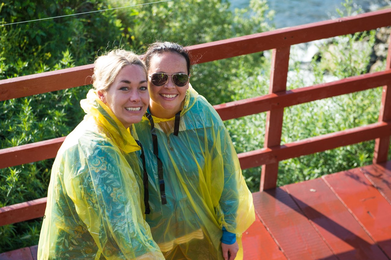 Two smiling women wearing yellow rain ponchos stand on a wooden walkway, posing for a photo.