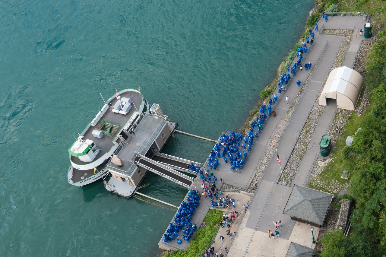 A tour boat is docked as a large group of people in blue ponchos wait to board.