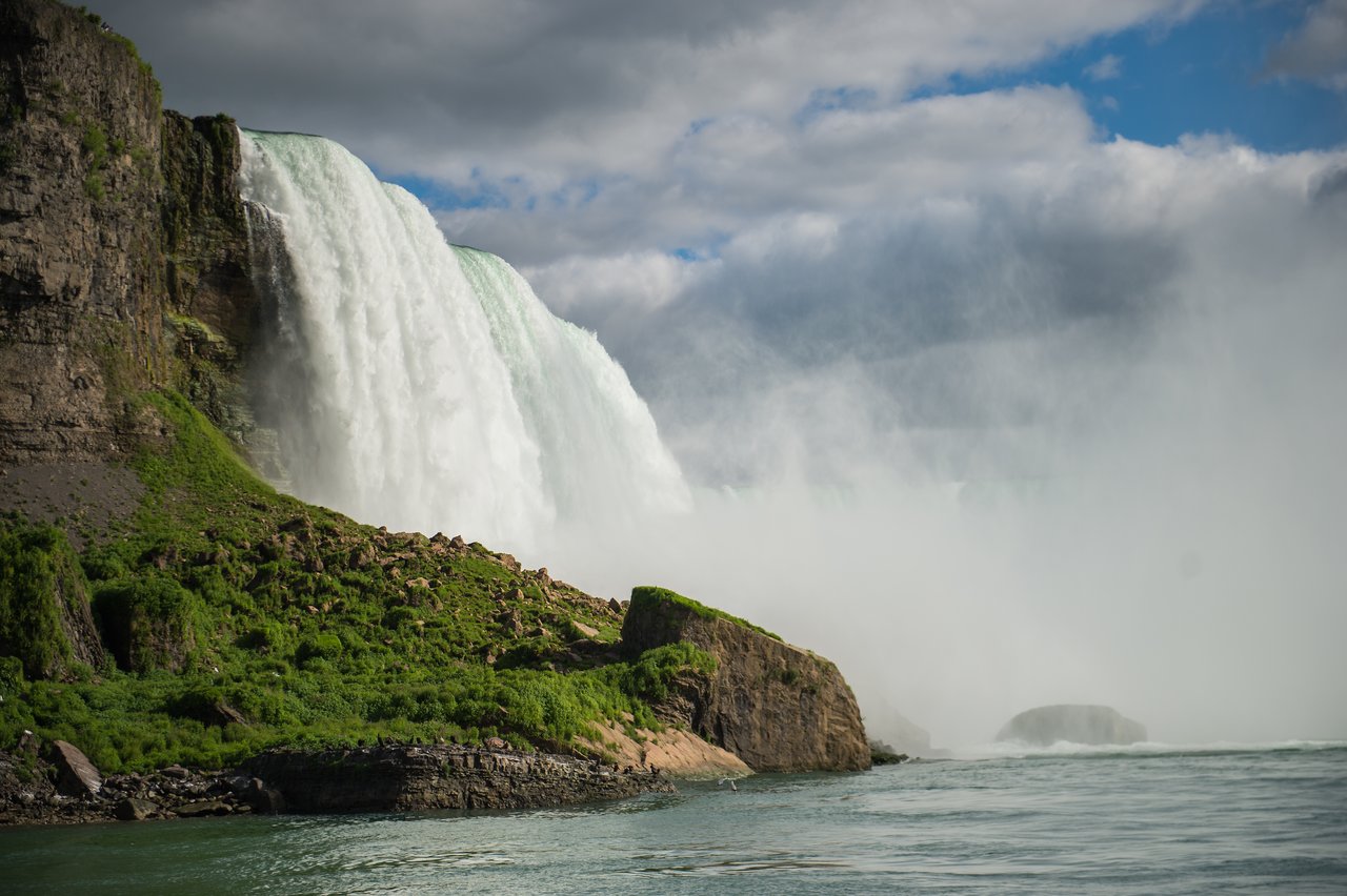 A large waterfall cascades over a rocky cliff, creating mist above the water below.