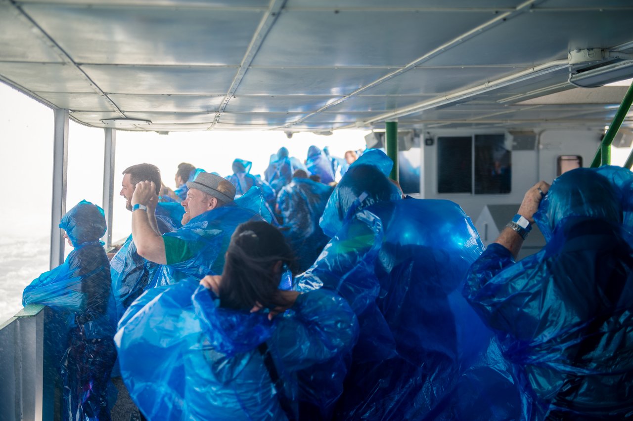 A group of people wearing blue rain ponchos stand on a boat, looking out at the water.