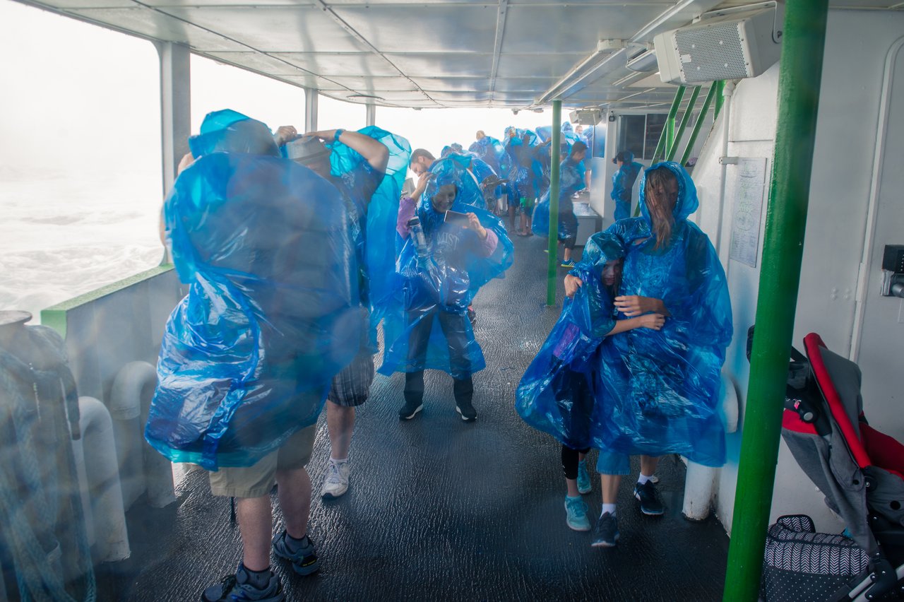 People wearing blue rain ponchos stand on a wet boat deck, shielding themselves from wind and water spray.