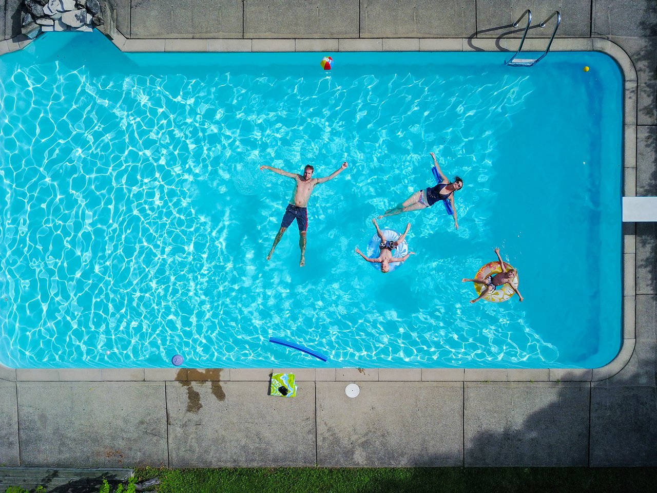 Four people float in a swimming pool, some on inflatable rings, while one person spreads their arms in the water.
