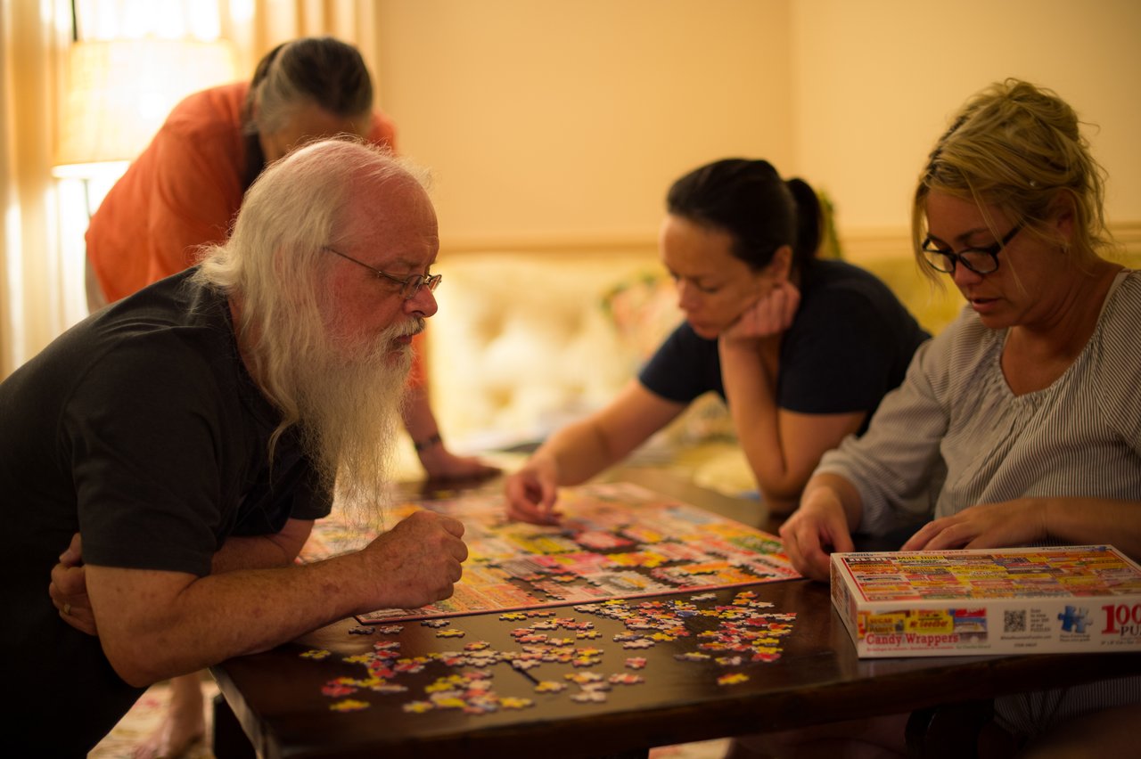 Four people work together on a colorful jigsaw puzzle at a table, focusing on finding and placing pieces.