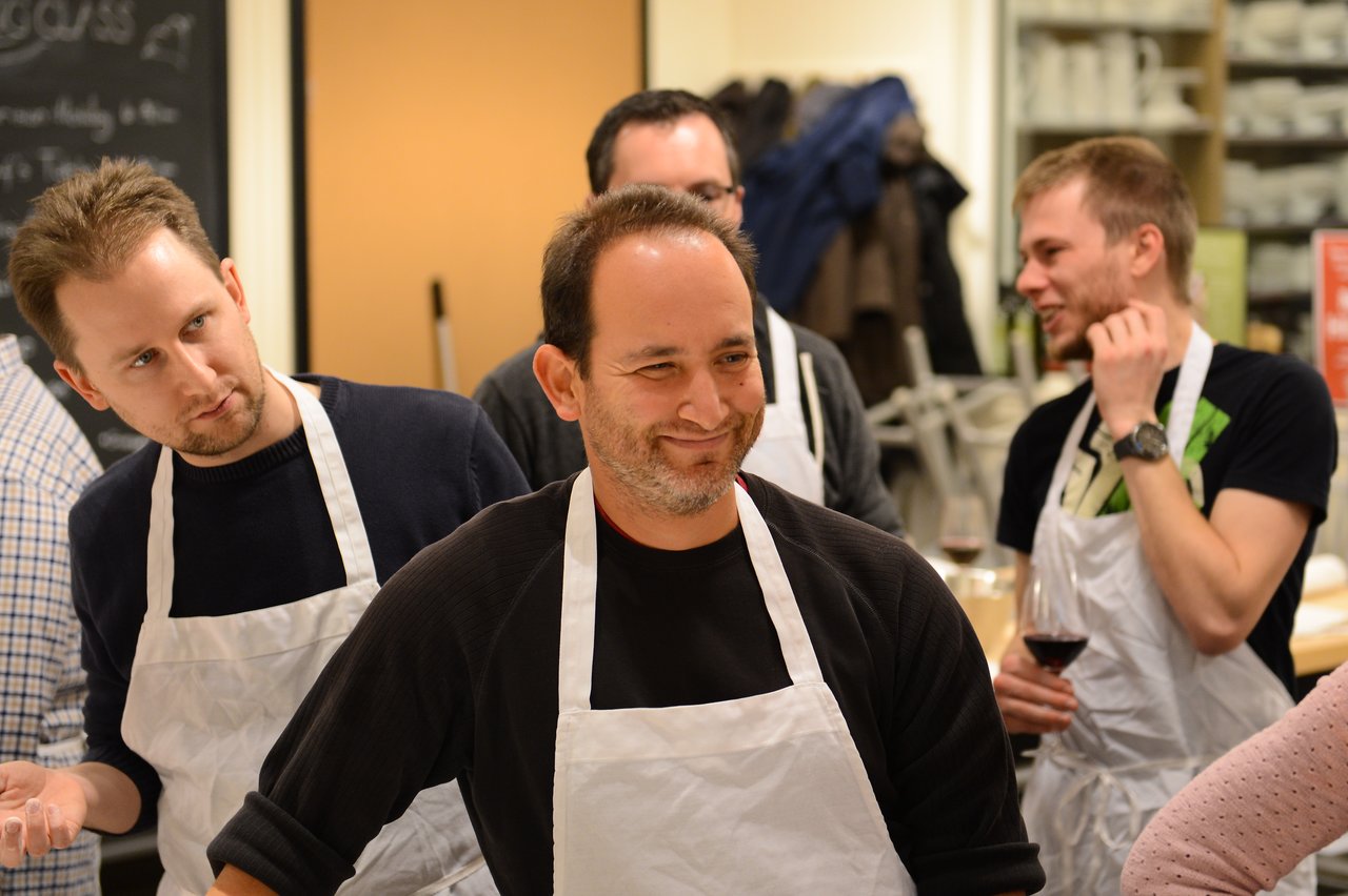 A group of people wearing aprons participate in a cooking class, engaging and interacting with each other.
