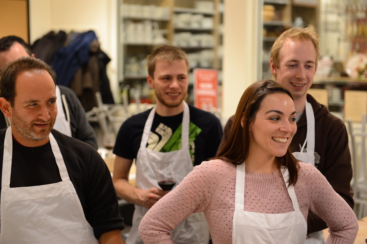 A group of people wearing aprons smile and engage in a cooking class.