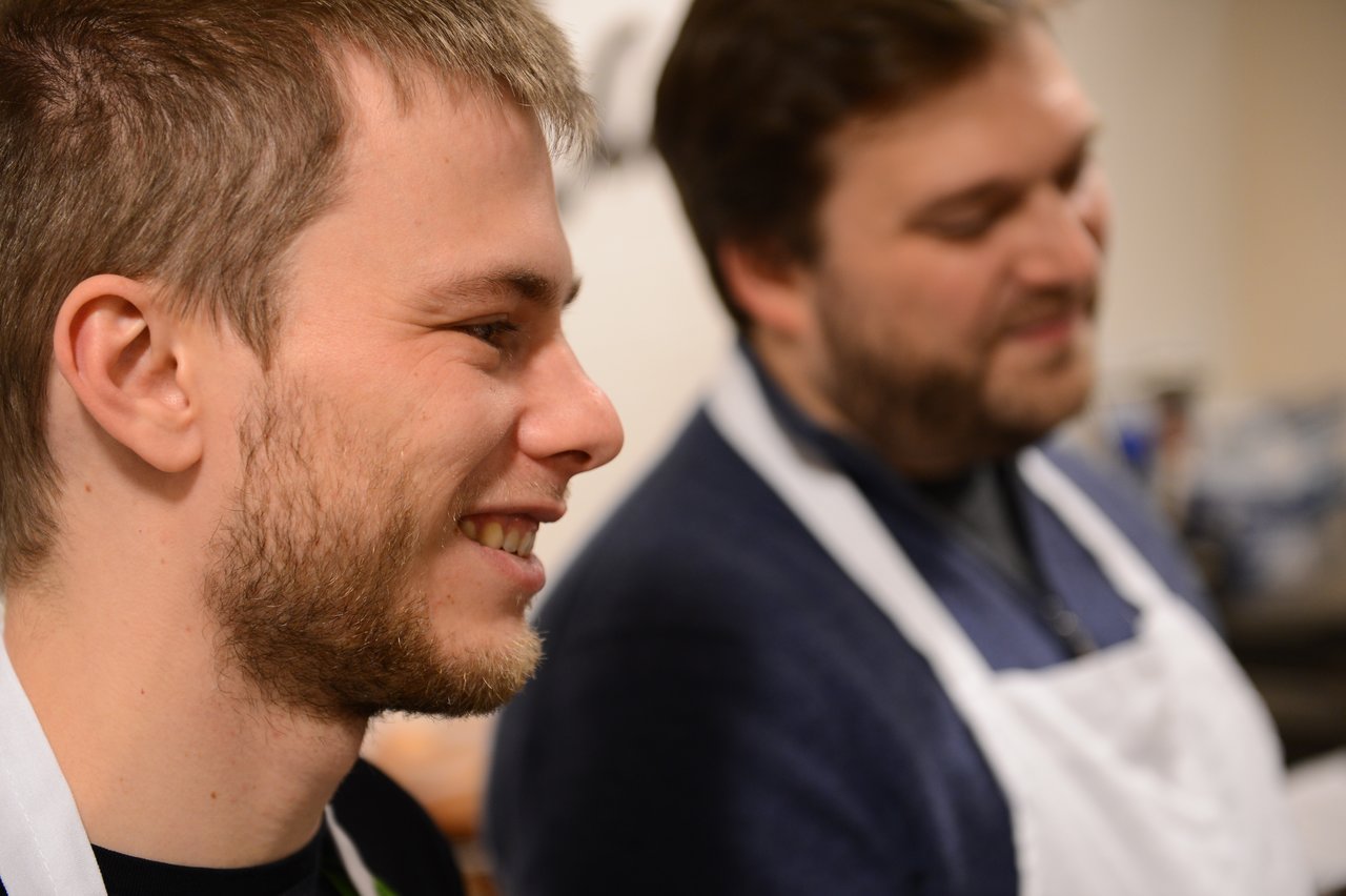 Two people wearing aprons smile while participating in a cooking class.