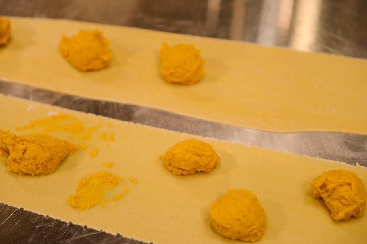 Dollops of orange filling placed on sheets of pasta dough, prepared for making stuffed pasta.