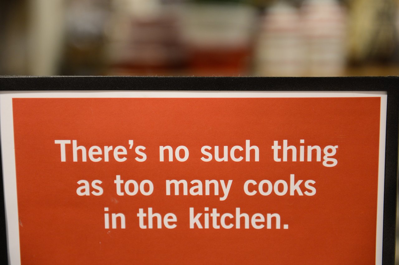 A sign with white text on a red background reads, "There's no such thing as too many cooks in the kitchen.