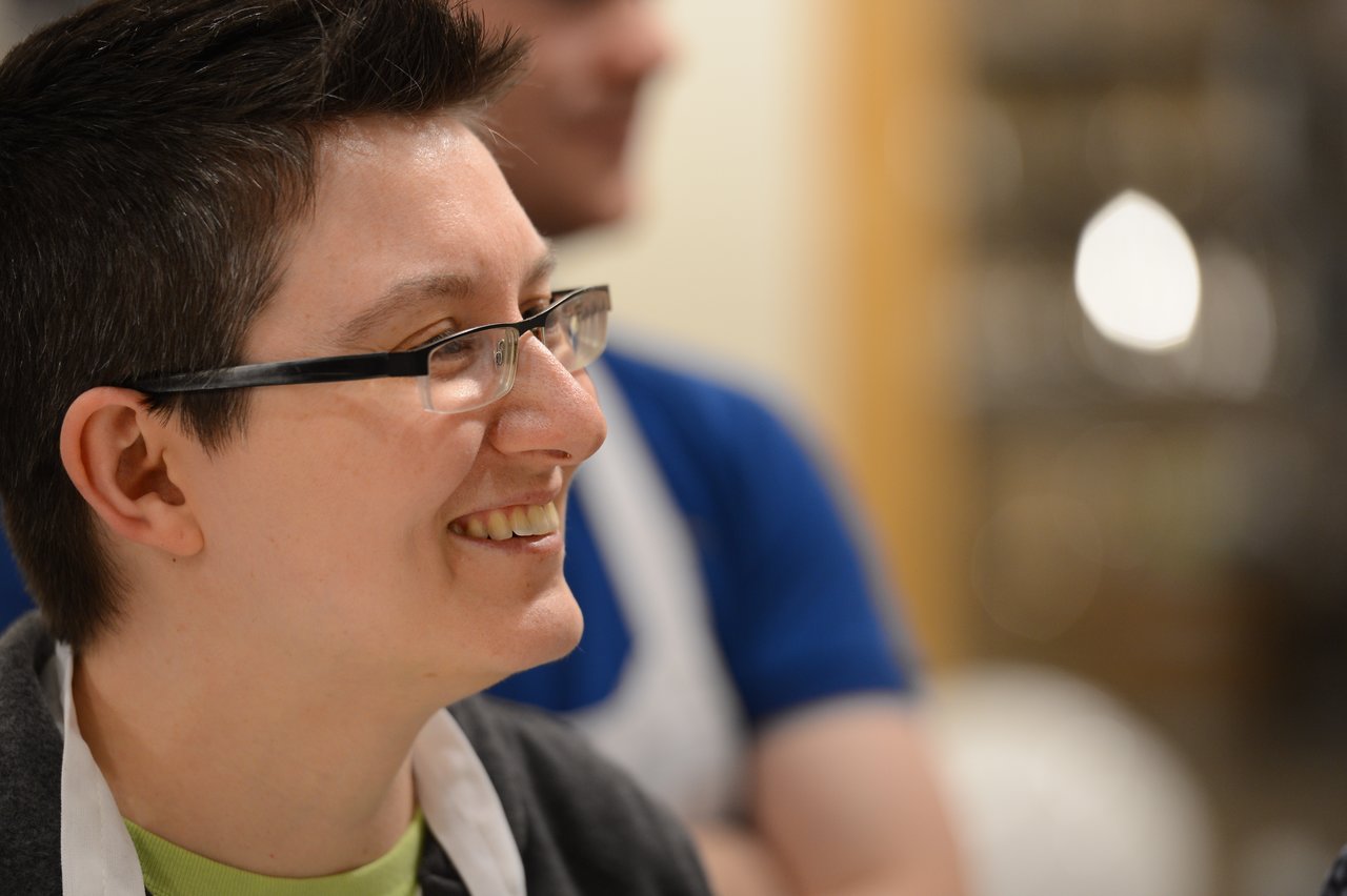 A person wearing glasses and an apron smiles while participating in a cooking class.