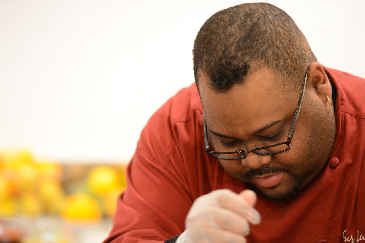 A chef in a red uniform and gloves focuses on preparing food in a cooking class.