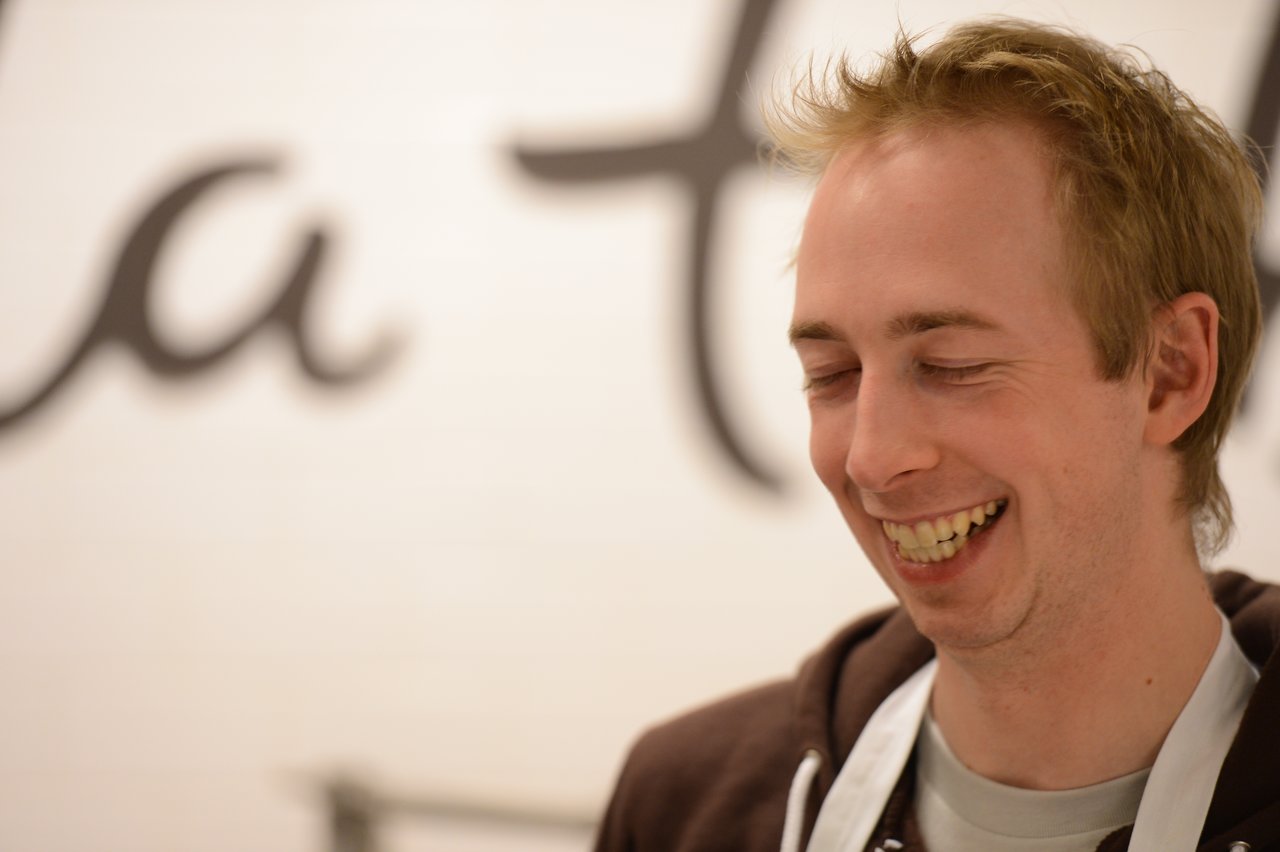 A person wearing a white apron smiles with eyes closed, possibly during a cooking class.