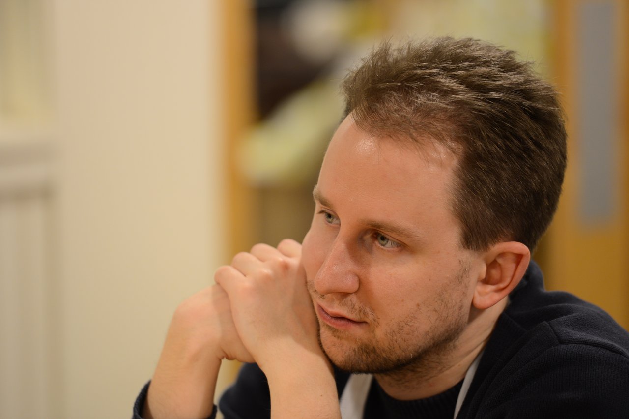 A person wearing a dark sweater and apron rests their chin on their hands, appearing focused during a cooking class.