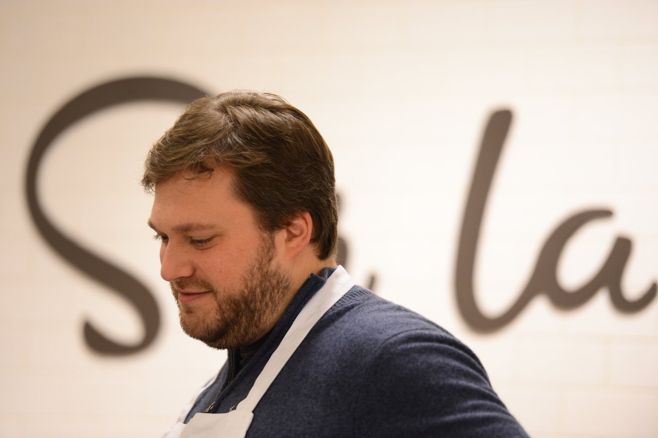 A man wearing a white apron looks down while participating in a cooking class.