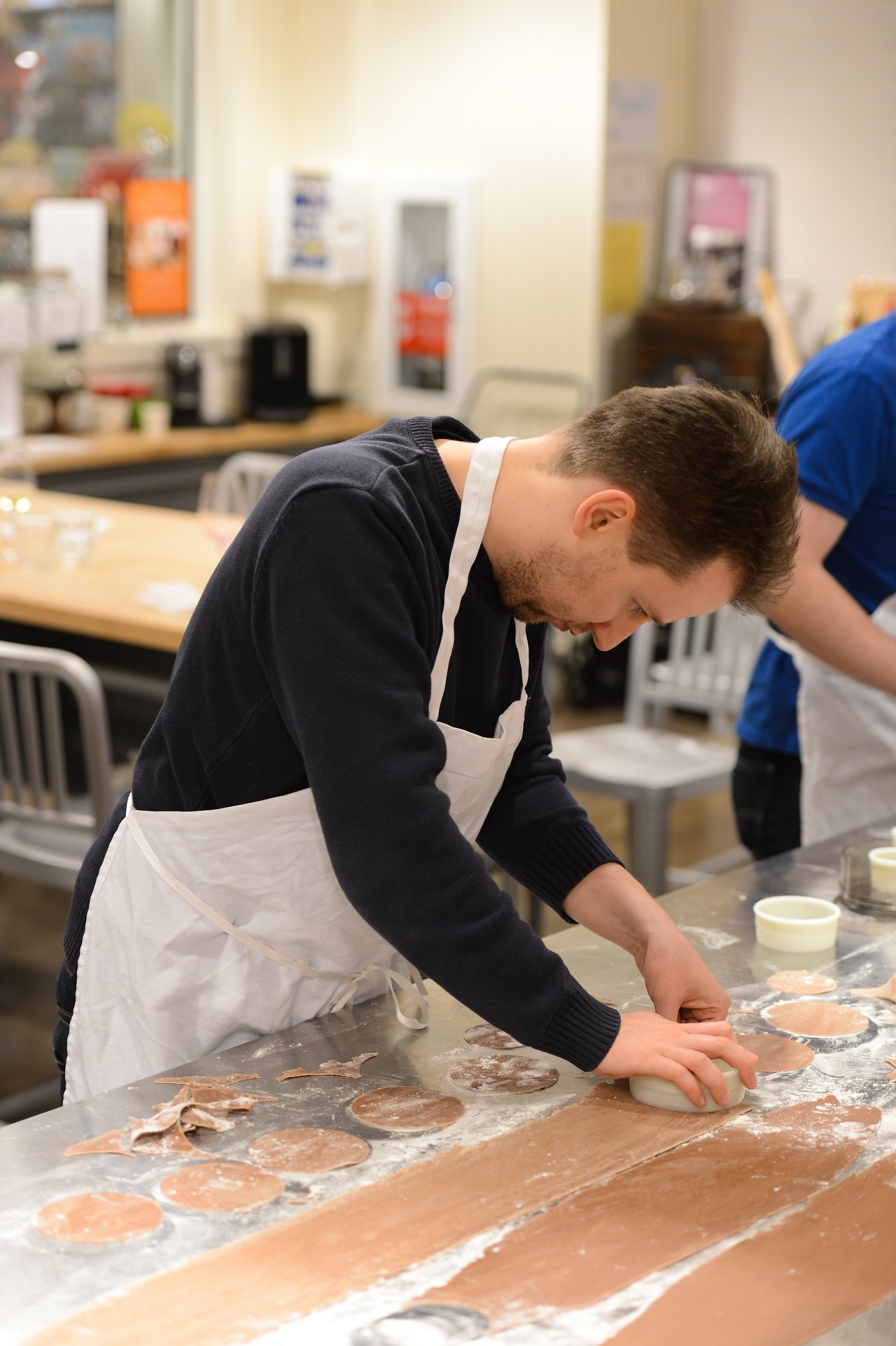 A person wearing an apron cuts circular shapes from rolled dough on a floured countertop in a cooking class.
