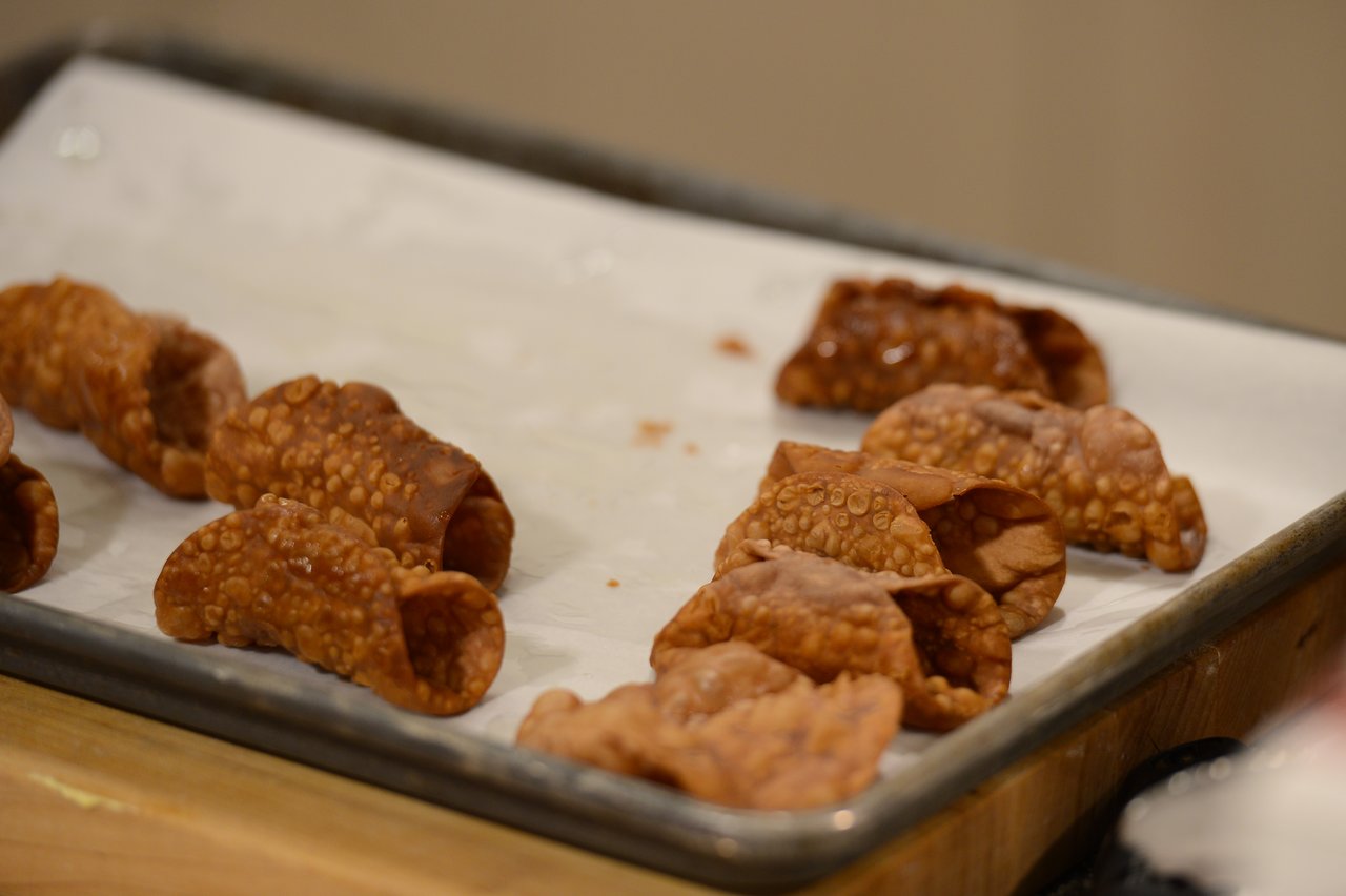 Golden-brown cannoli shells cooling on a parchment-lined baking sheet, ready to be filled.