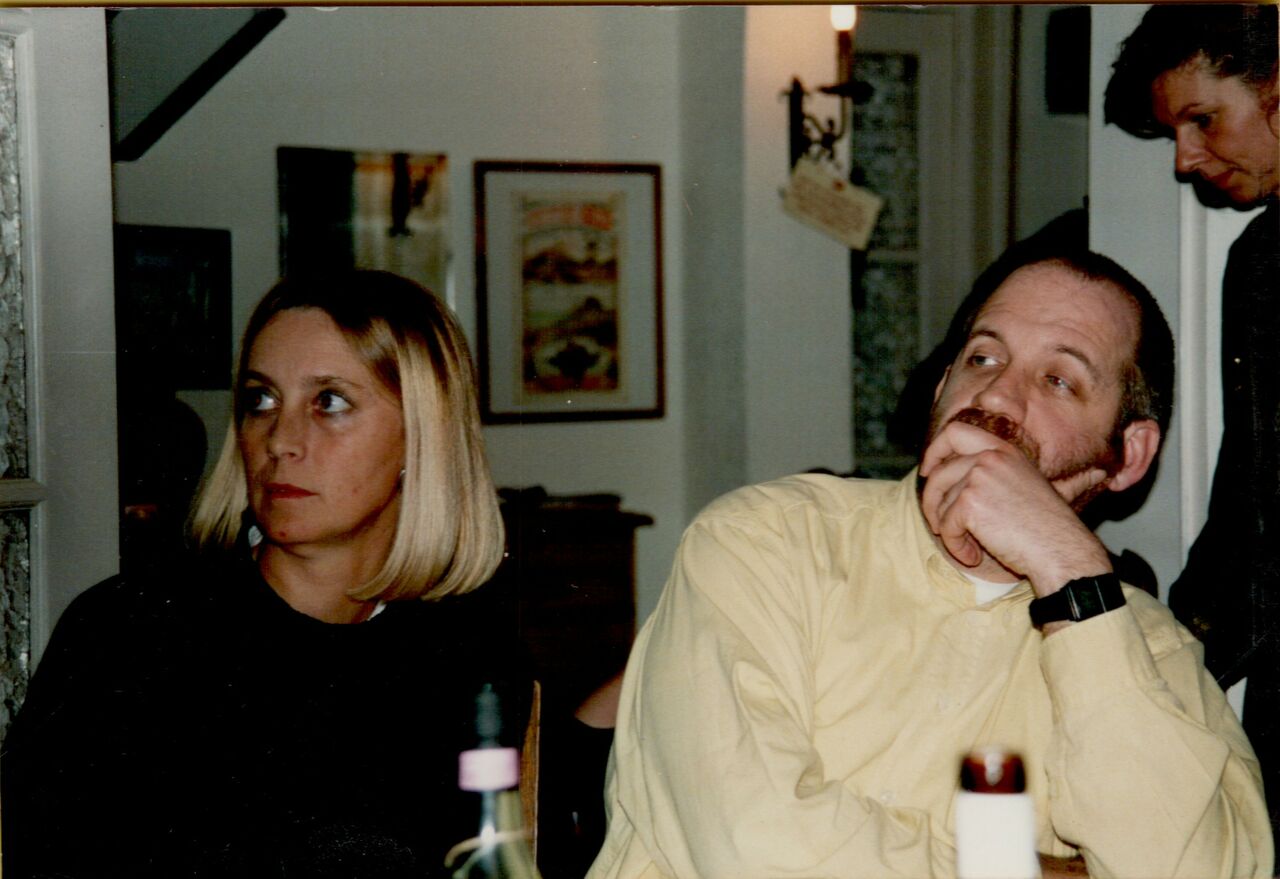 A woman and a man sit at a table, both looking in different directions with serious expressions.