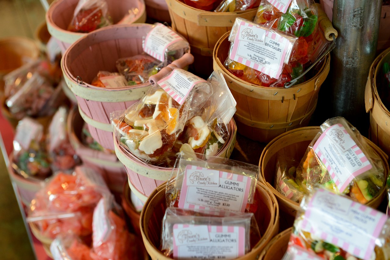 Baskets filled with packaged gummy candies, including gummy alligators and gummy dinosaurs, displayed in a candy store.