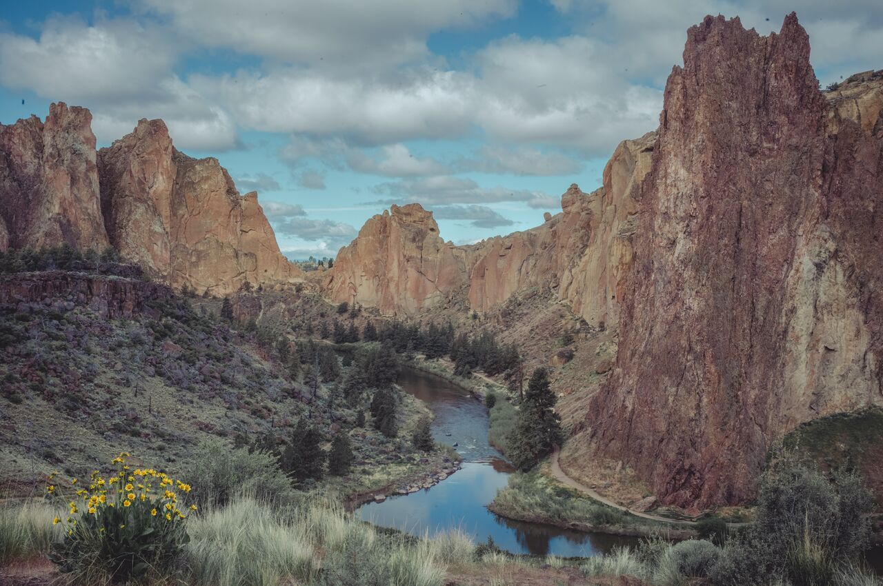 Tall rock cliffs surround a winding river and hiking trail at Smith Rock State Park in Oregon.