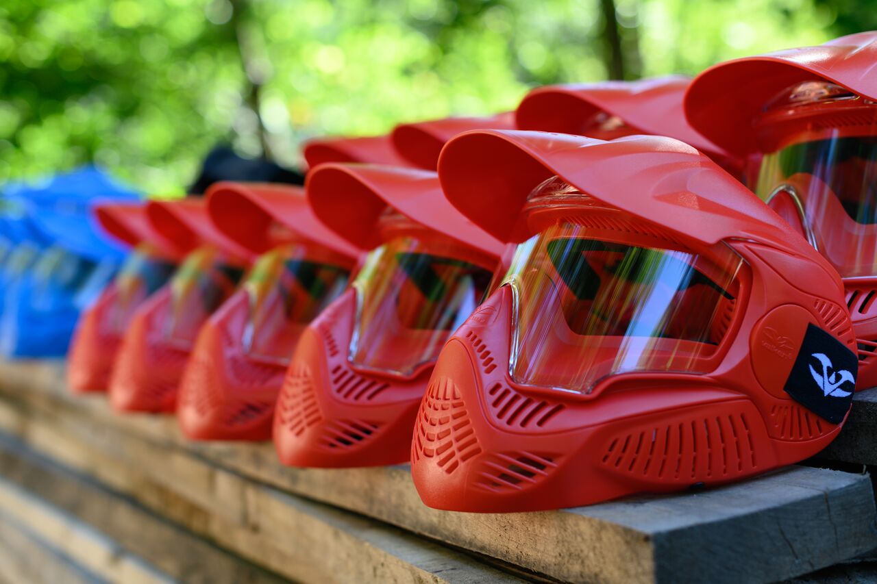 Rows of red and blue paintball masks neatly arranged on a wooden surface, ready for use.